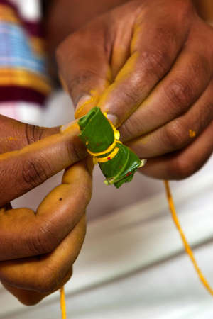 A Hindu priest prepares an areca nut wrapped in a betel leaf as part of a Bengali pre-wedding ceremonyの写真素材