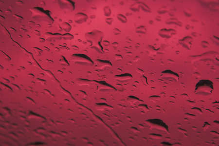 Rain drops on window with red backgroundの写真素材