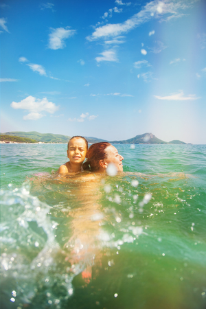 Mother and daughter swim in the beautiful sea, enjoy and have fun on vacationの写真素材