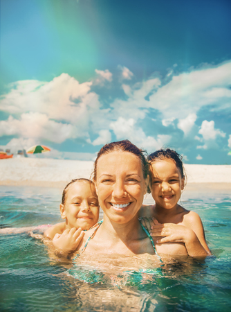 Mother and daughter swim in the shallow sea. They laugh and enjoy on a beautiful beach.の写真素材