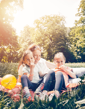 Mother and daughters in the park. They sit on the grass, laugh and enjoy their free time.の写真素材