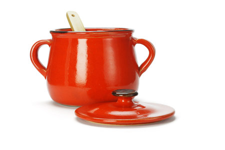 Open red clay pot with wooden ladle on white background