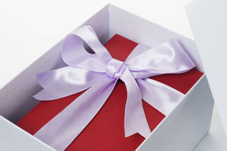 Close up of red giftbox with bow ribbon inside open white box on isolated backgroundの写真素材