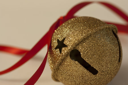 Macro view of a golden sleigh bell Christmas ornament tied with red ribbon.の写真素材