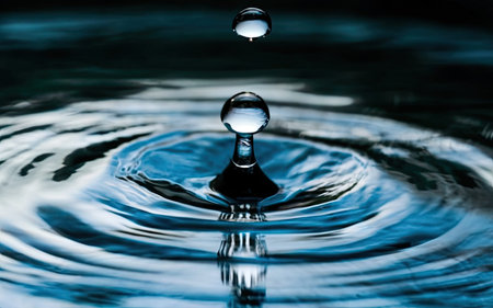 Water drop falling into water with ripples and waves in the backgroundの素材