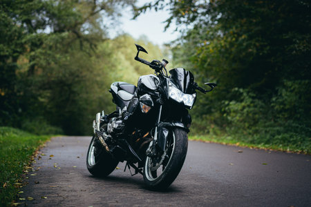 Black sports motorcycle standing on a forest road on a background of green trees