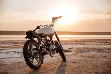 Retro motorcycle standing on the beach at sunset