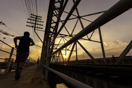 evening time view of a man runnig along siluate old steel bridge structure and railway, rama6 Bangkok Thailand, 1926の写真素材