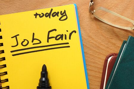 Notepad with job fair on a wooden table.の写真素材