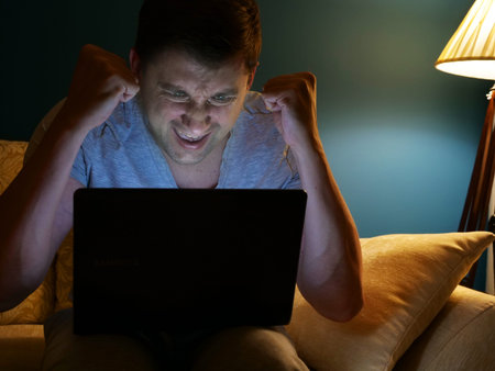 Happy man watching something on a laptop. Winning. Evening activities at home.