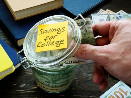 Savings for college. Hand puts money in a glass jar.の写真素材