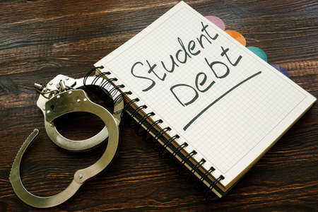 Student debt handwritten sign in the notebook and handcuffs.の写真素材