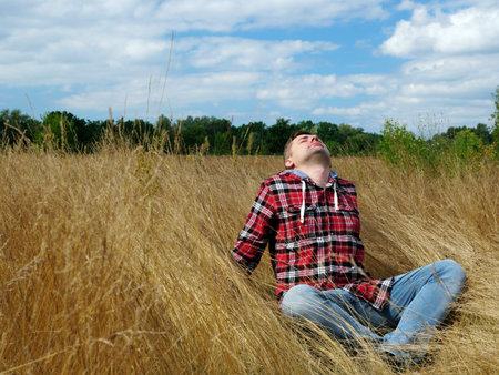 A young guy is sitting in the autumn grass. Relaxation and tourism in nature.