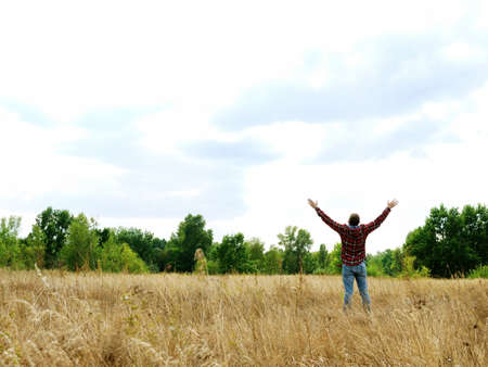 A man in an autumn field stretches out his hands to the sky.の写真素材