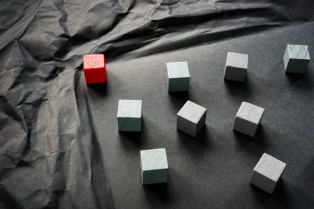 Leadership and overcoming difficulties. Red cube as leader and gray ones on dark paper.の写真素材