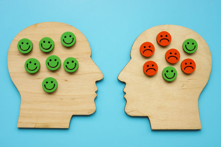 Wooden outlines of heads, happy and sad smiles. Stress, negative emotions and psychotherapy concept.