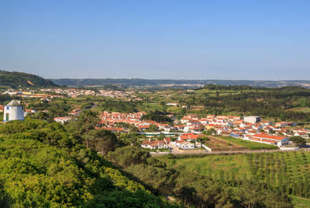 Scenic view of the valley from wall of fortress. White houses red tiled roofs Beautiful old town with medieval. Obidos village, Portugal. Summer sunny day.  Popular tourist destination.のeditorial素材