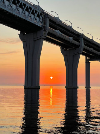 Beautiful sunset over the sea. The sun setting between the pillars of the bridge. Reflection of sunlight on water. The sky is painted in golden colors. Kanonersky Island, Saint-Petersburg.の写真素材