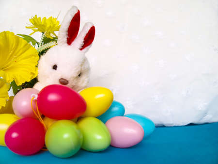 White plush rabbit with colorful Easter eggs and yellow flowers. Empty space for text.の写真素材