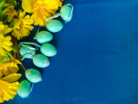 Easter eggs on blue silk, with yellow flowers. Empty space for text.の写真素材