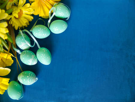 Easter eggs on blue silk, with yellow flowers. Empty space for text.の写真素材