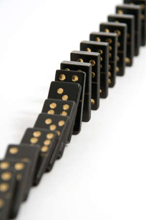 A line of black dominoes falling down, isolated on a white background with a narrow depth of field.の写真素材