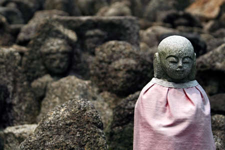 A small statue of the Buddhist saint Jizo, amongst roughly carved & weathered rocks.の写真素材