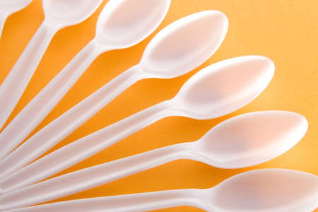 White plastic spoons arranged on an orange background.の写真素材