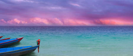 exotic ocean panorama with a colorful cloudscape and boats with a parrot in similar, harmonic colors                           の写真素材