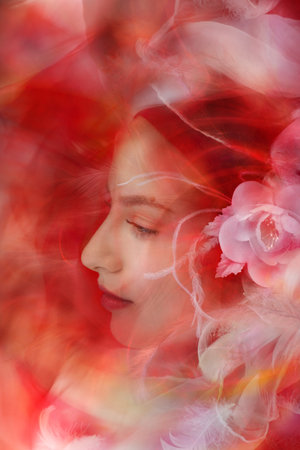 A gently looking lady is looking through white, transparent feathers like through a peaceful dream.の写真素材