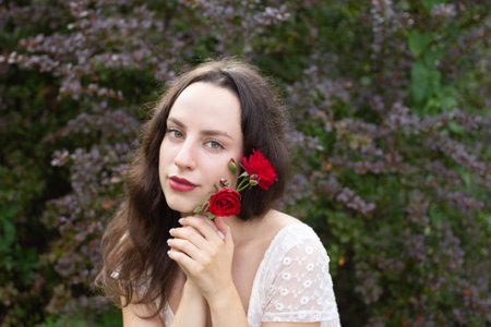A lovely woman holds wild roses in her hands, while expressing a charming look.の写真素材