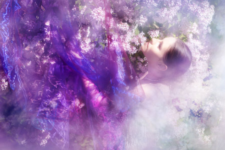 A woman behind a veil, over a lightful beauty bush at springtime looks upwards in bright light.の写真素材