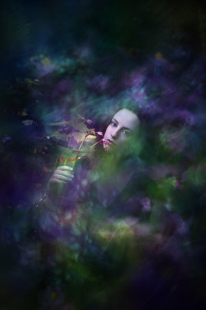 Beauty portrait of a woman, holding a begonia flower on a dark background.