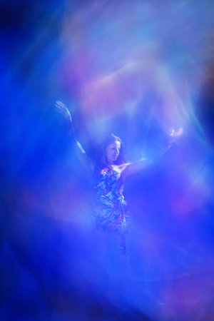 Woman in a Tulip petals dress is openly standing with wide arms, directed to heaven, where an ethereal light appearance hovers above her to symbolize spiritual belief.の写真素材