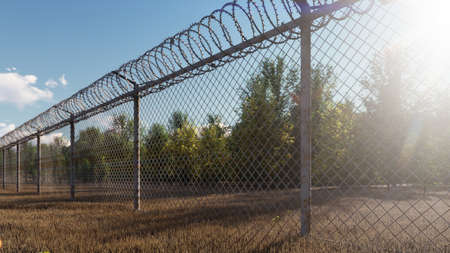 The suns rays and autumn trees are visible through the metal prison fence with barbed wire. 3D Renderingの写真素材