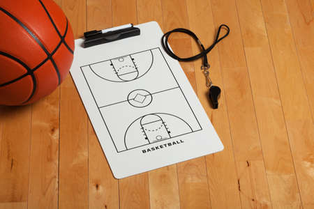 A basketball with coach's clipboard and whistle on a wooden gymnasium floorの写真素材