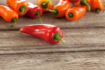 A red sweet pepper with other peppers behind it on a rough wood surface shot at a low angle with selective focusの写真素材