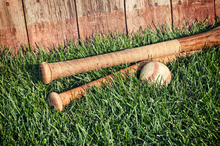 Vintage baseball and bats lying in grass in front of an old fenceの写真素材