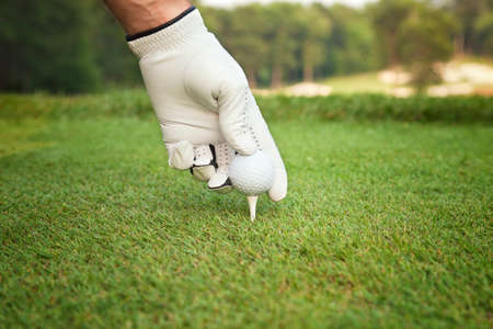 A selective focus, low angle view of a golfer's gloved hand placing a ball on a teeの写真素材
