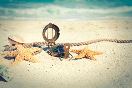 Cross-processed, selective focus compass with shells and rope on an ocean beachの写真素材