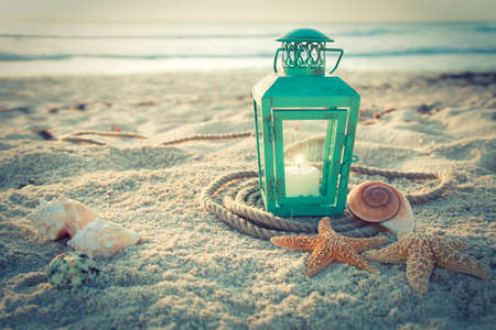 Cross-processed lantern on the beach with shells and rope at sunriseの写真素材
