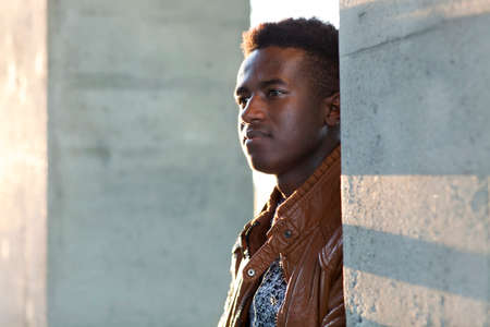 Handsome young black man stands in sunlight between concrete pillarsの写真素材