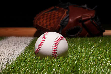 Baseball on grass field low angle close up with mitt and bat soft focus behindの写真素材