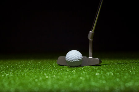 Low angle selective focus of golf ball and putter on a green with black backgroundの写真素材