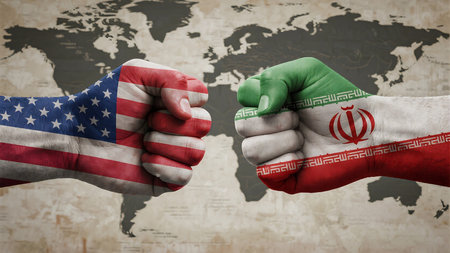 The image features two clenched fists facing each other, with the United States flag painted on the left fist and the flag of Iran on the right fist. This symbolic representation is set against a world map. The composition conveys a sense of international conflict, tension, or rivalry between the two nations. The world map is rendered in a desaturated style, making the brightly colored flags on the fists the central focus.の写真素材
