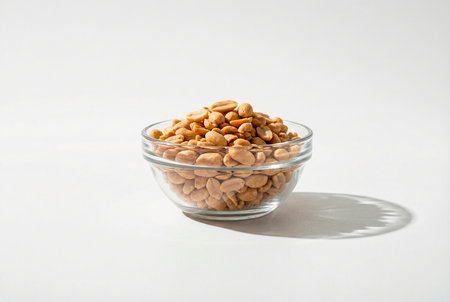 Salted peanuts in a glass bowl on a white background with shadowsの素材