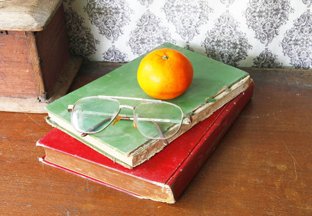 still life with old bookglasses and orange on wooden table.の写真素材