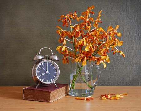 still life with jug of orchidold book and clock on wooden table.の写真素材