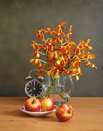 still life with jug of orchidapple and clock on wooden table.の写真素材