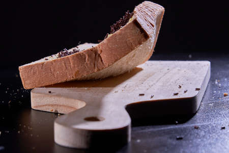 A slice of bread spread chocolate sprinkled onto the wooden board, isolated on black background.の写真素材